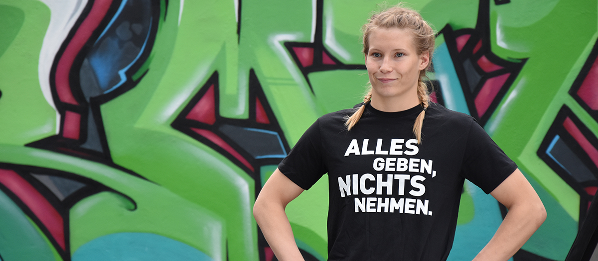 Ringerin Aline Focken im Initiativ-Shirt vor einer Graffiti-Wand